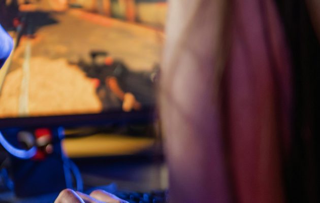 Adult woman focused on playing video game using a keyboard and headset indoors.