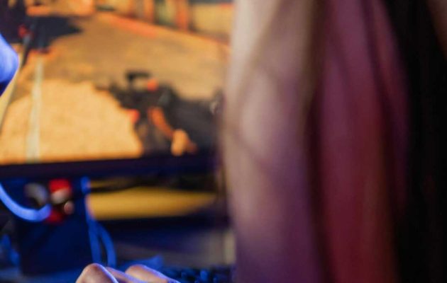 Adult woman focused on playing video game using a keyboard and headset indoors.