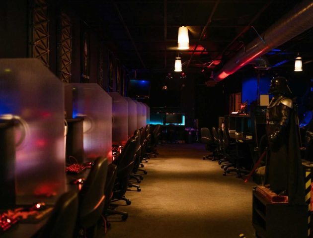 A dimly lit gaming arcade with neon lights and computers, creating a futuristic atmosphere.