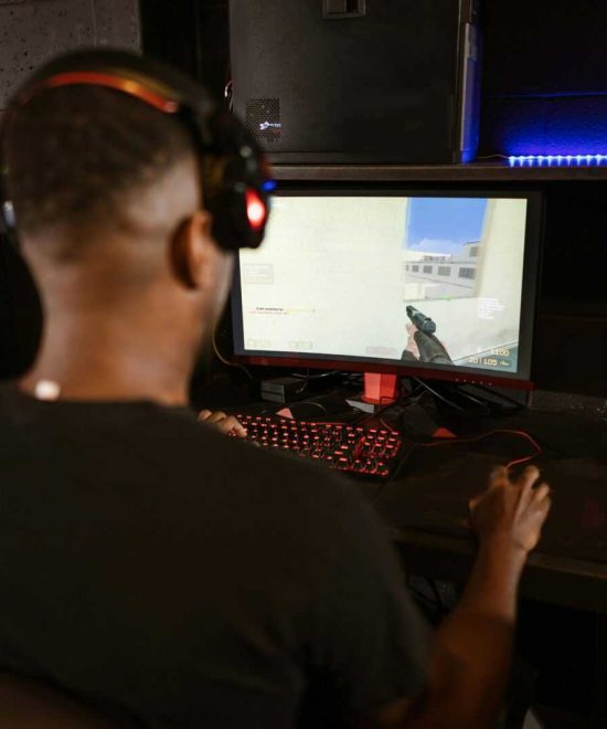 A man deeply engaged in a video game at a modern esports setup with multiple screens.