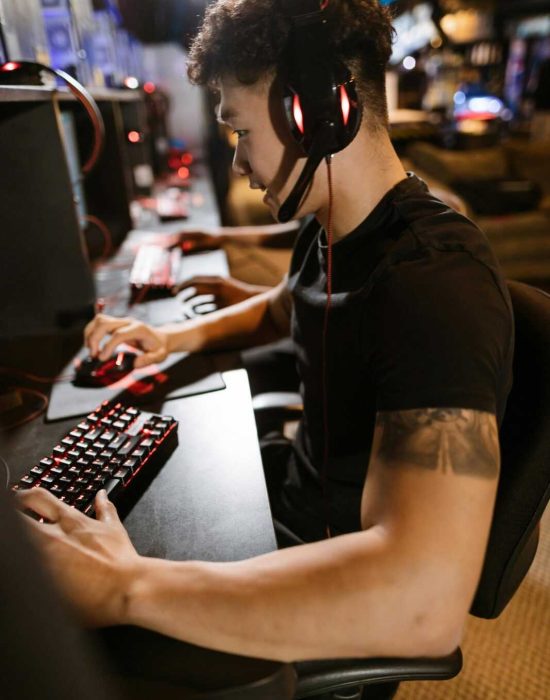 A gamer wearing headphones intensely focused on gaming in a cyber-themed arcade.