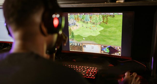 A gamer intensely playing a strategy game on a high-resolution monitor indoors.