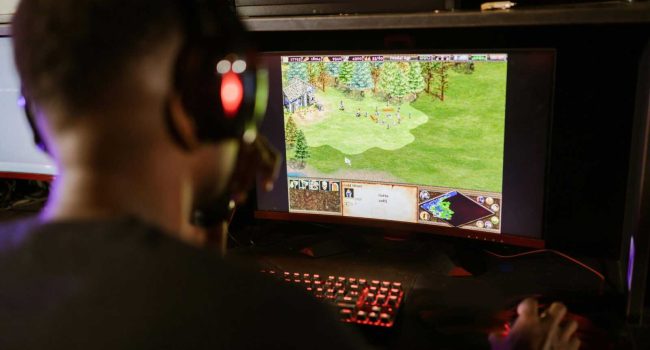 A gamer intensely playing a strategy game on a high-resolution monitor indoors.