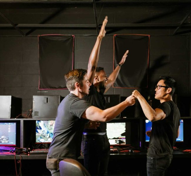 Three excited gamers celebrating their victory in an esports gaming arena, showing teamwork and joy.